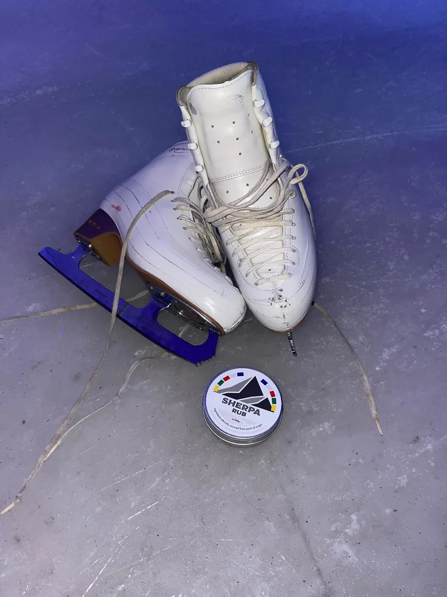 Figure skating boots on the ice beside a 100g tin of Sherpa Rub